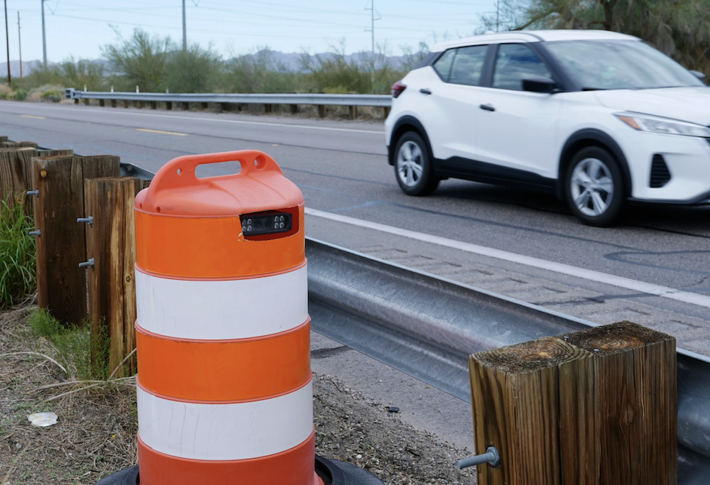 a photo from the AP story, showing a car traveling on a road next to a roadside traffic drum, in white and orange, showing a hidden license plate reader inside.