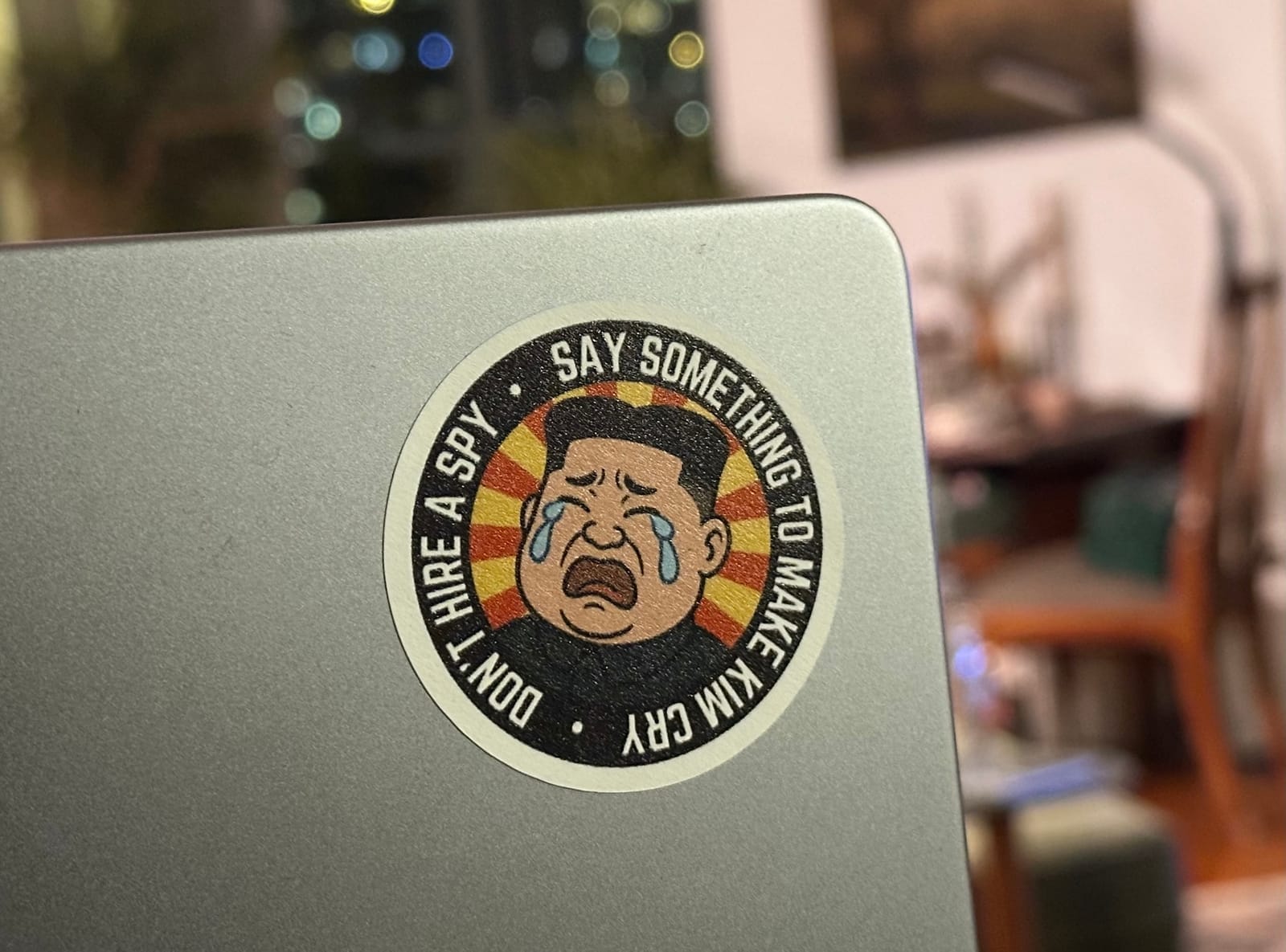 a sticker on a laptop with a cartoon photo of Kim Jong Un crying, with the words: "Don't hire a spy, say somethjing to make Kim cry."