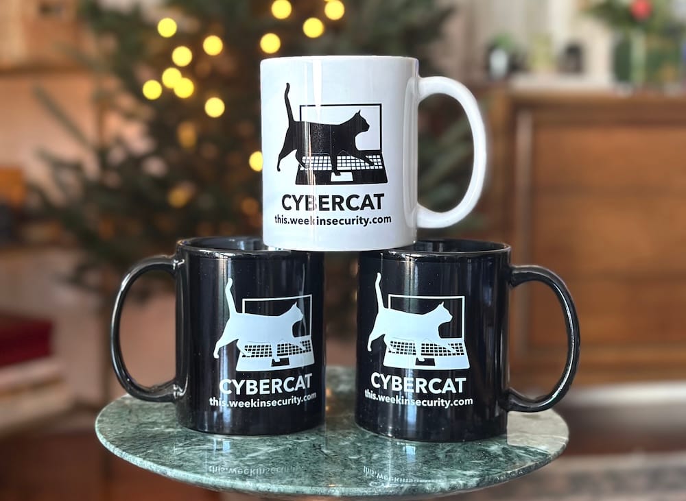 a photo of three cyber-cat themed 'this week in security' mugs, two black and one white, against a holiday tree background.