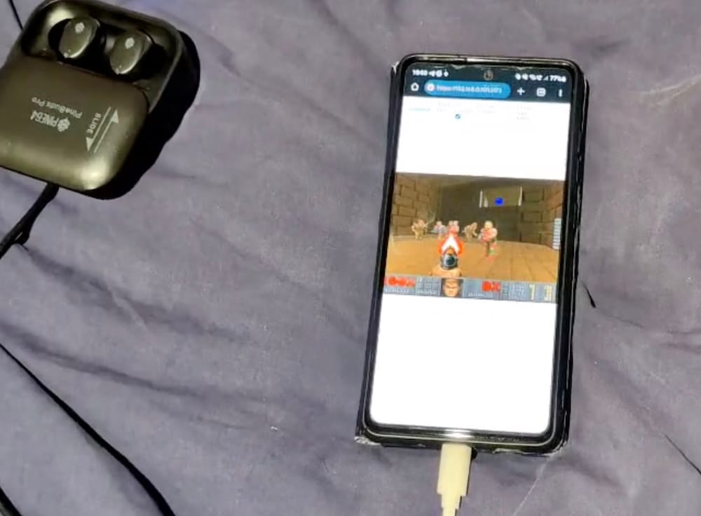 a photo of an Android phone with a web browsing running a web-version of Doom, connected by USB cable to a pair of Pinebuds Pro earbuds.